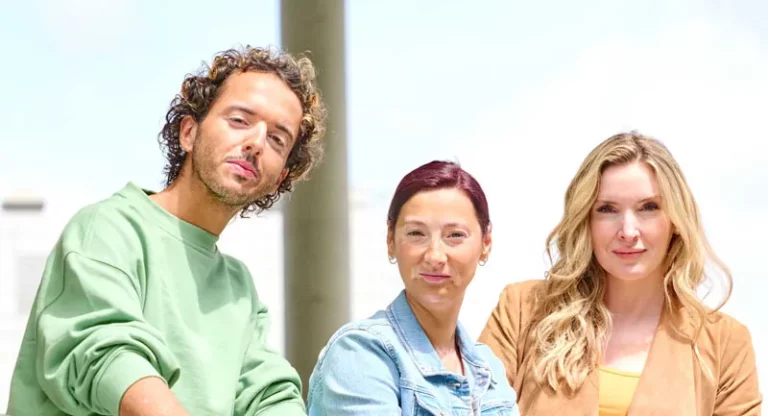 Ein Mann und zwei Frauen mit der Weissfleckenkrankheit Vitiligo stehen lächelnd nebeneinander
