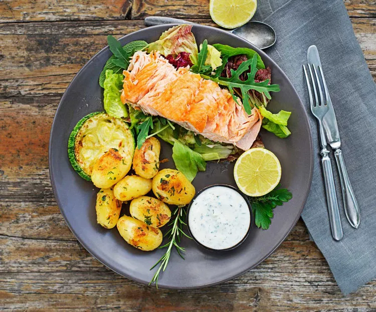 Schön angerichteter Teller mit einem gegarten Lachs Filet mit Ofen-Kartoffeln an Salatbouquet als Vitiligo-Sommerrezept mit antientzündlichem Potential und Quelle für Omega-3-Fettsäuren.